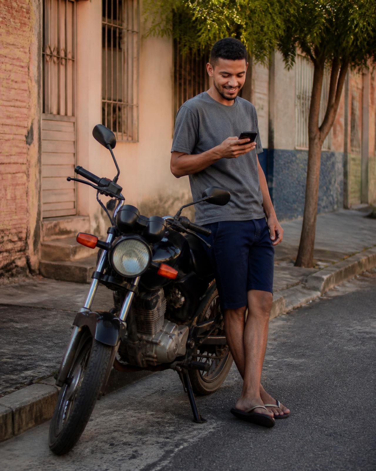 Jovem olhando o celular perto de uma moto estacionada na rua